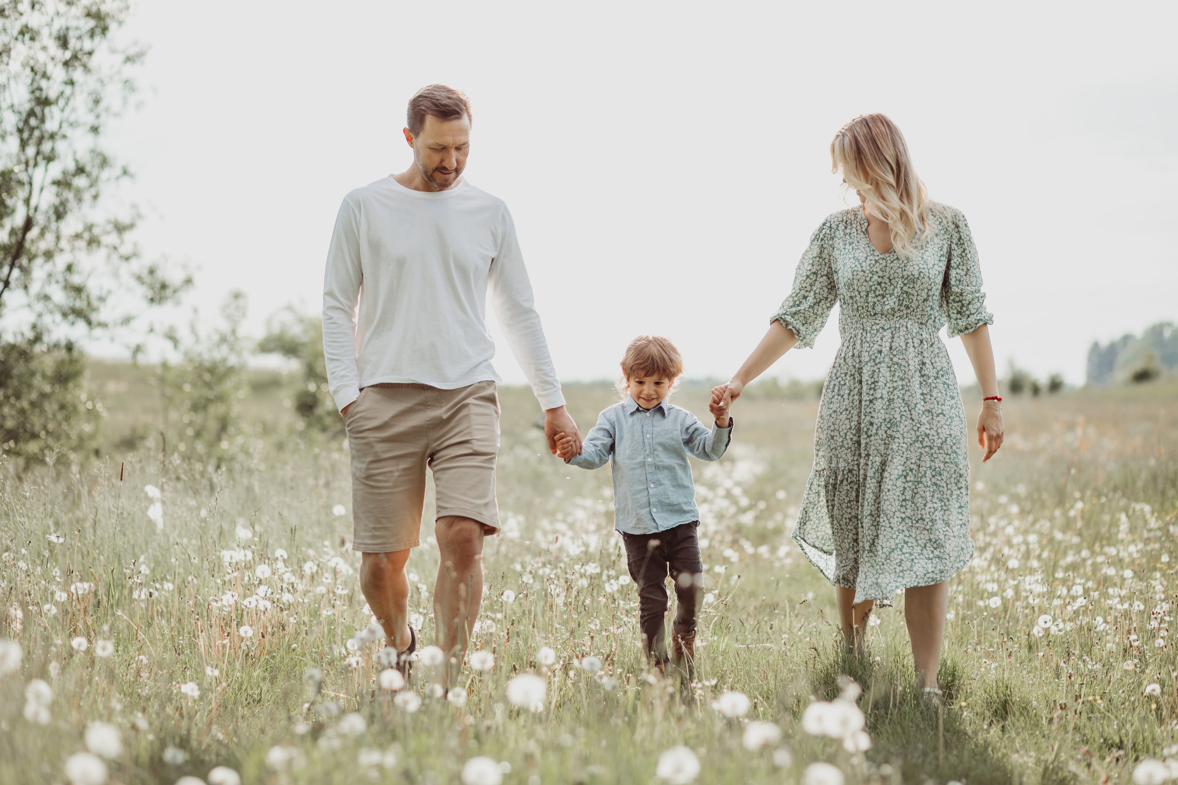 Two parents holding hands with their child walking through a field of dandelions