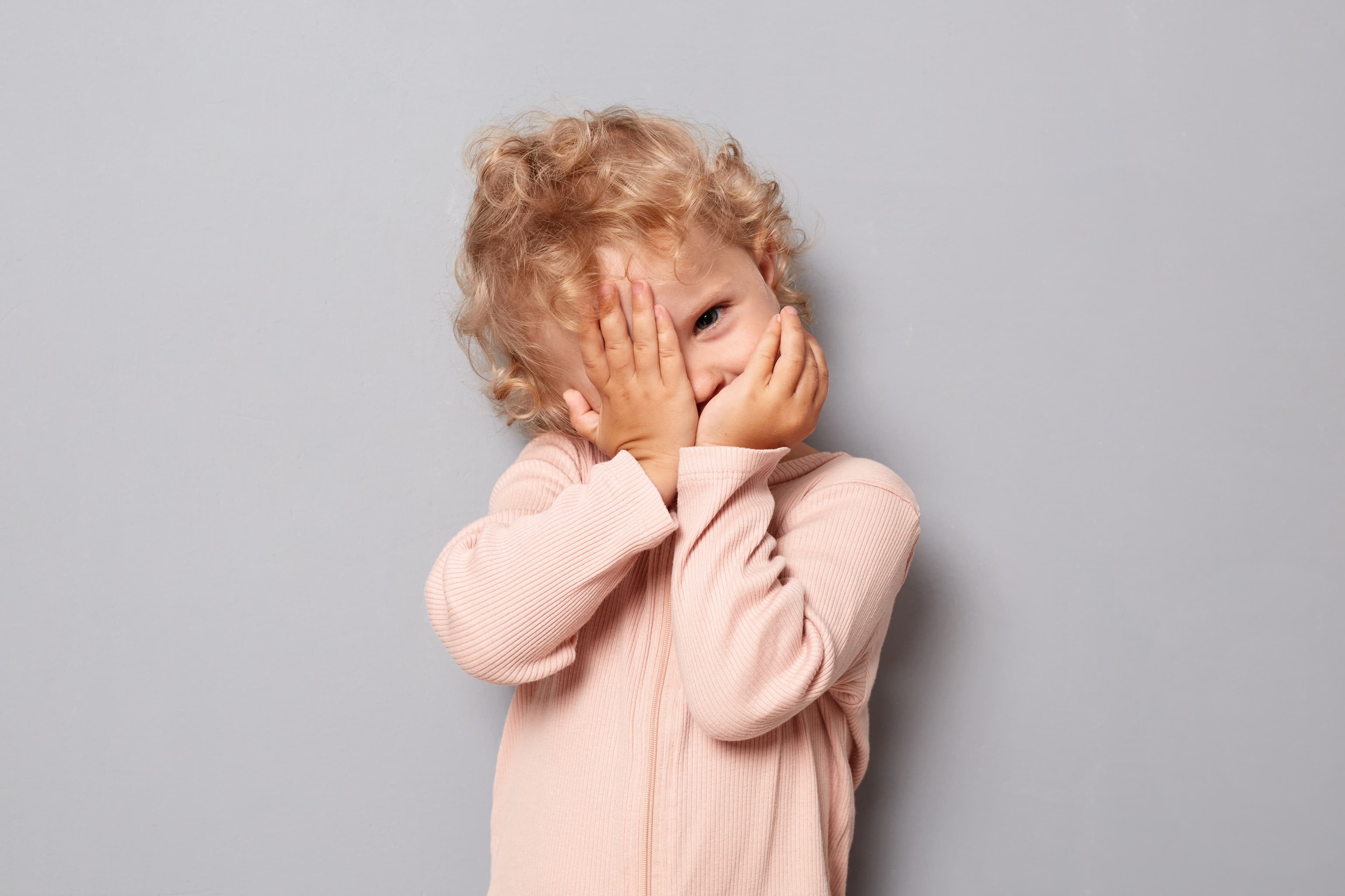 A child covering their face and mouth with their hands