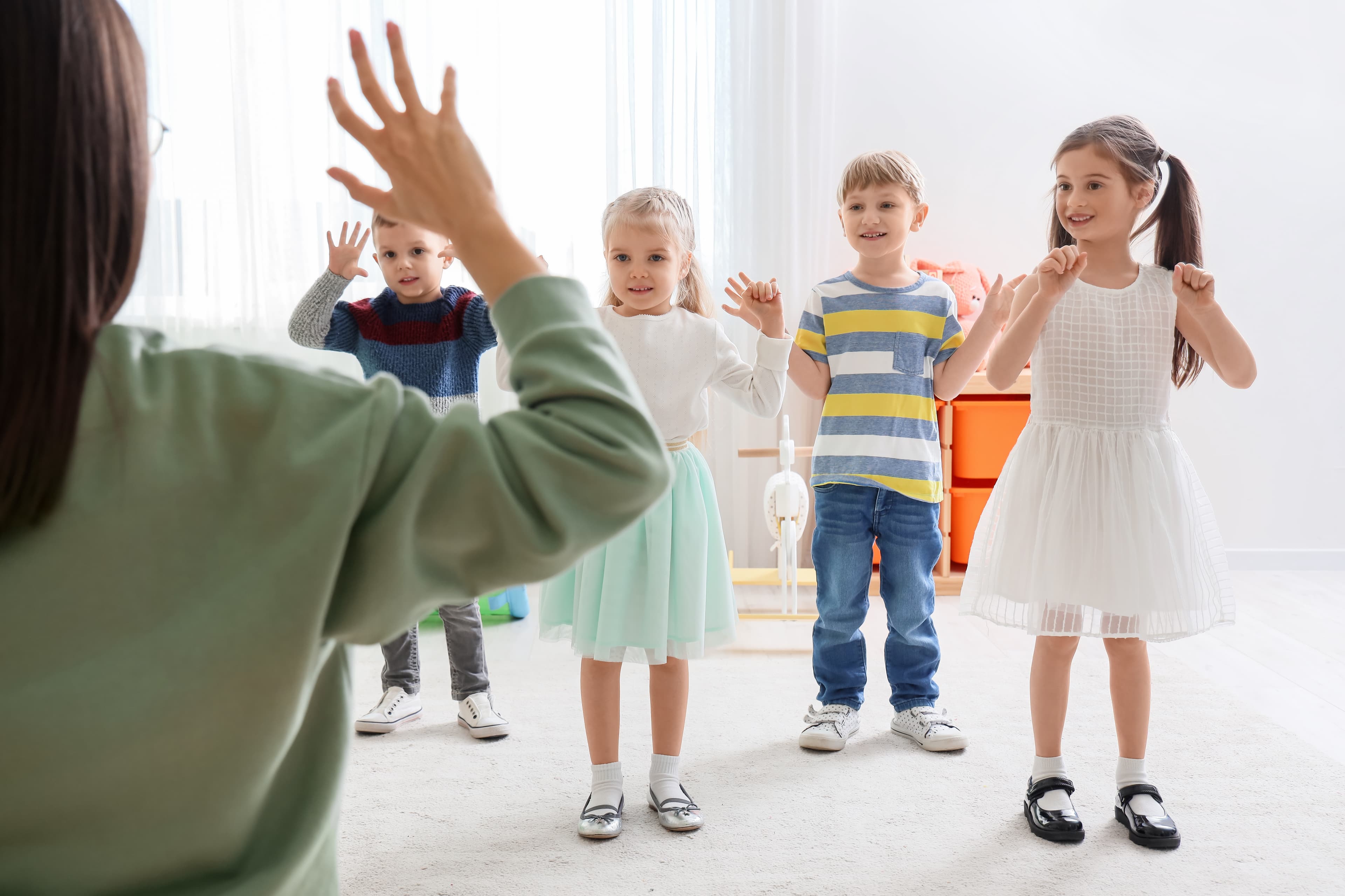 An adult in the foreground holding up 5 fingers with children in the background