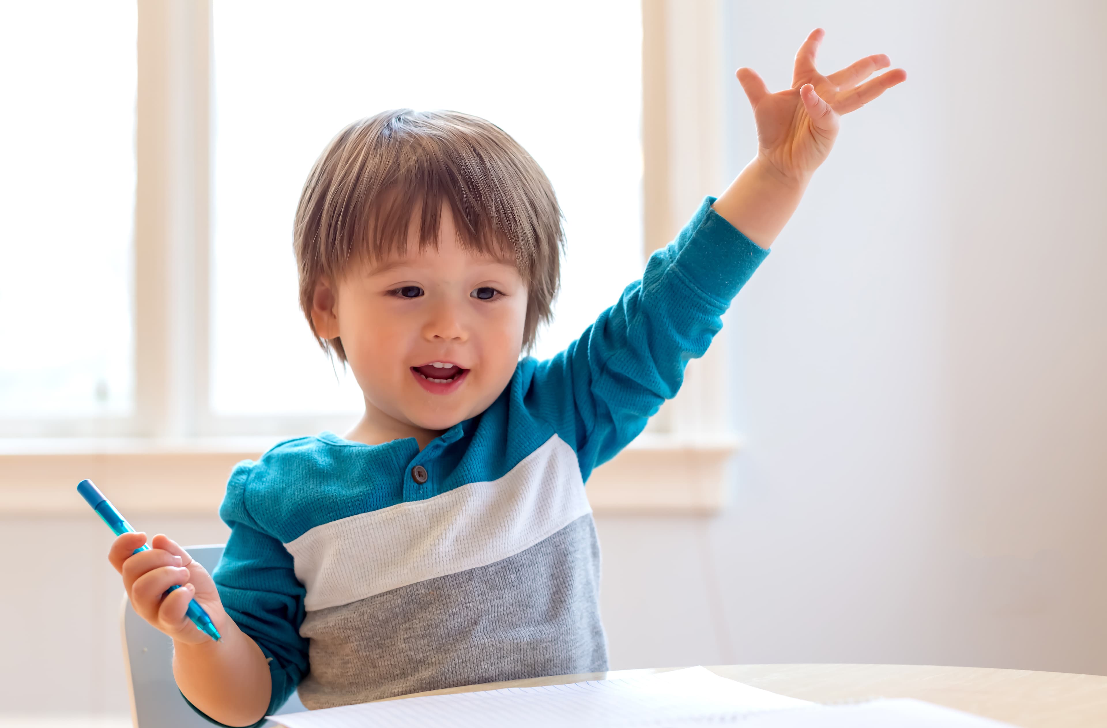 A child holding a pen in one hand smiling with an outstetched arm
