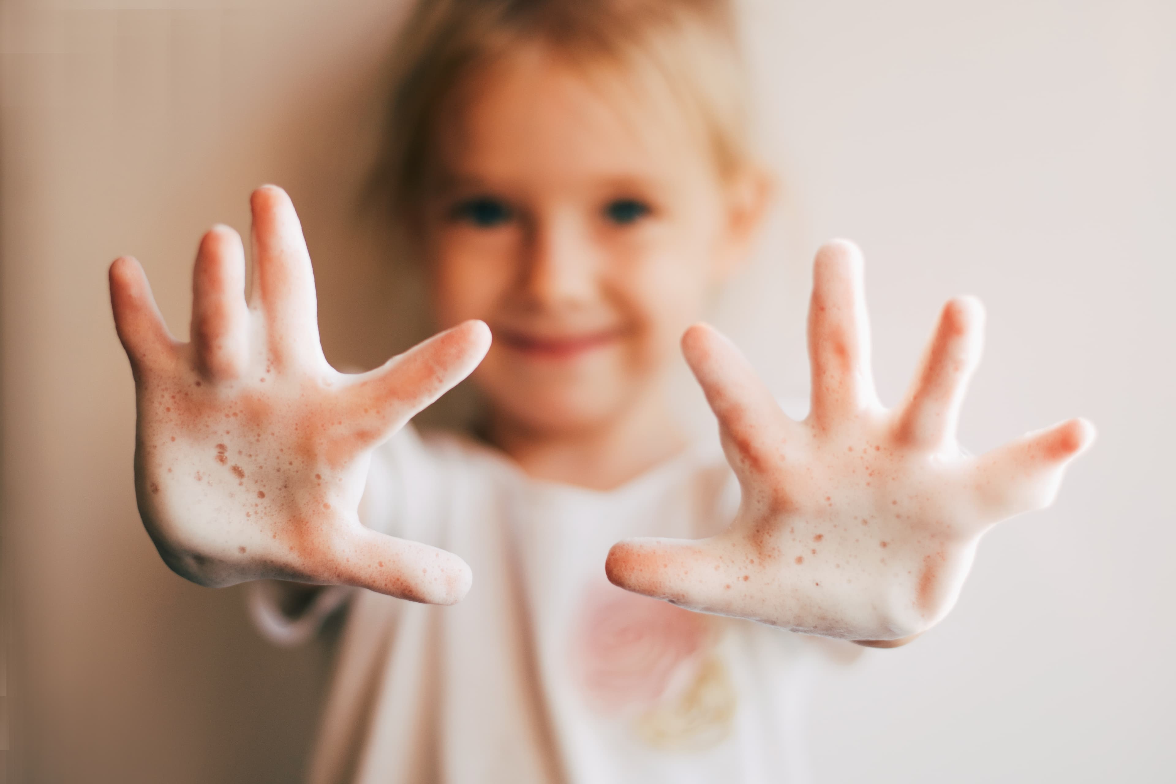 A girl holding up outstetched hands covered in soapy bubbles