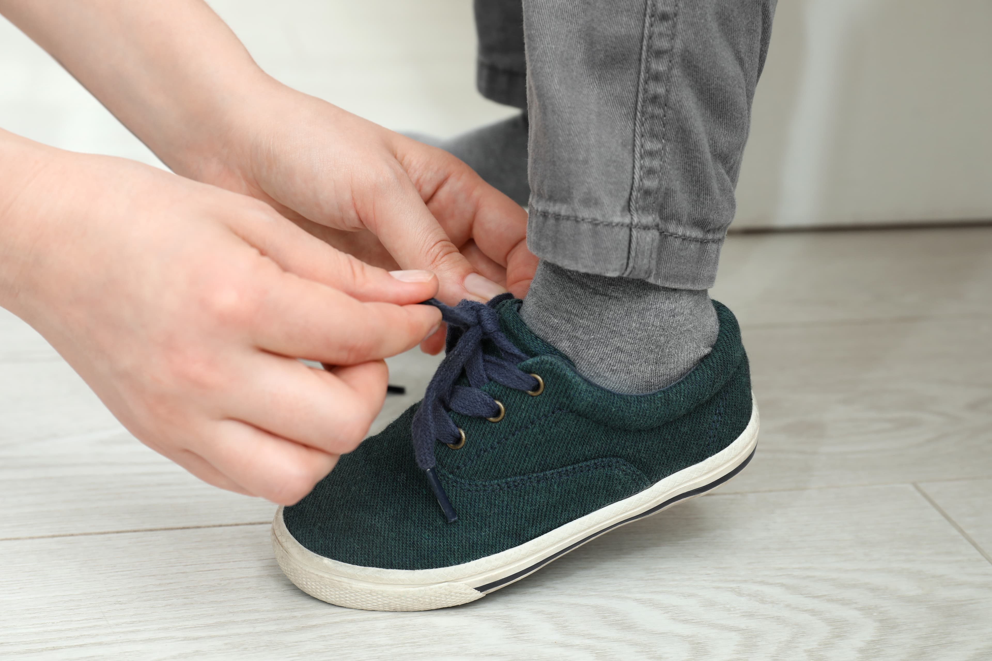 An adult's hand tying a child's shoelaces