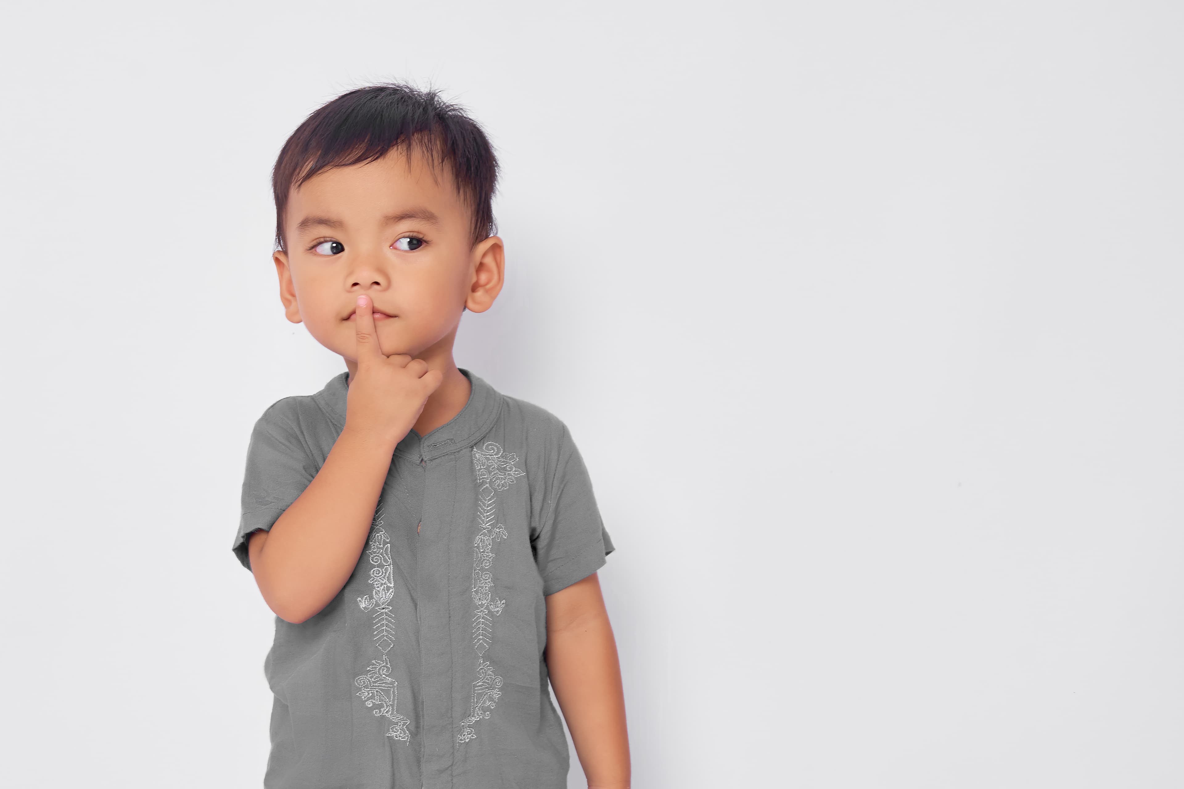 A child holding their finger to their mouth and looking pensively to the right