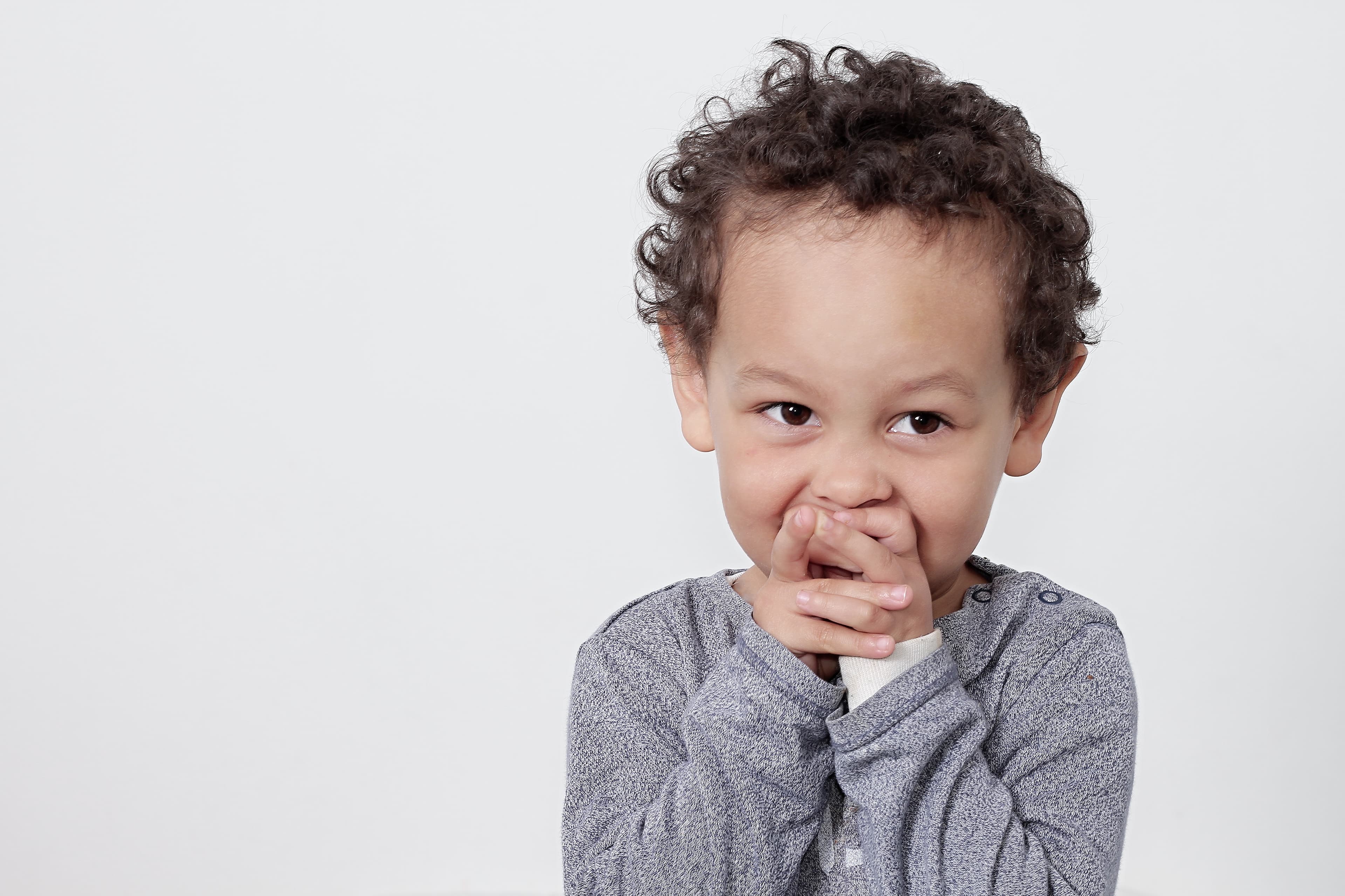 A smiling child covering their mouth with their hands