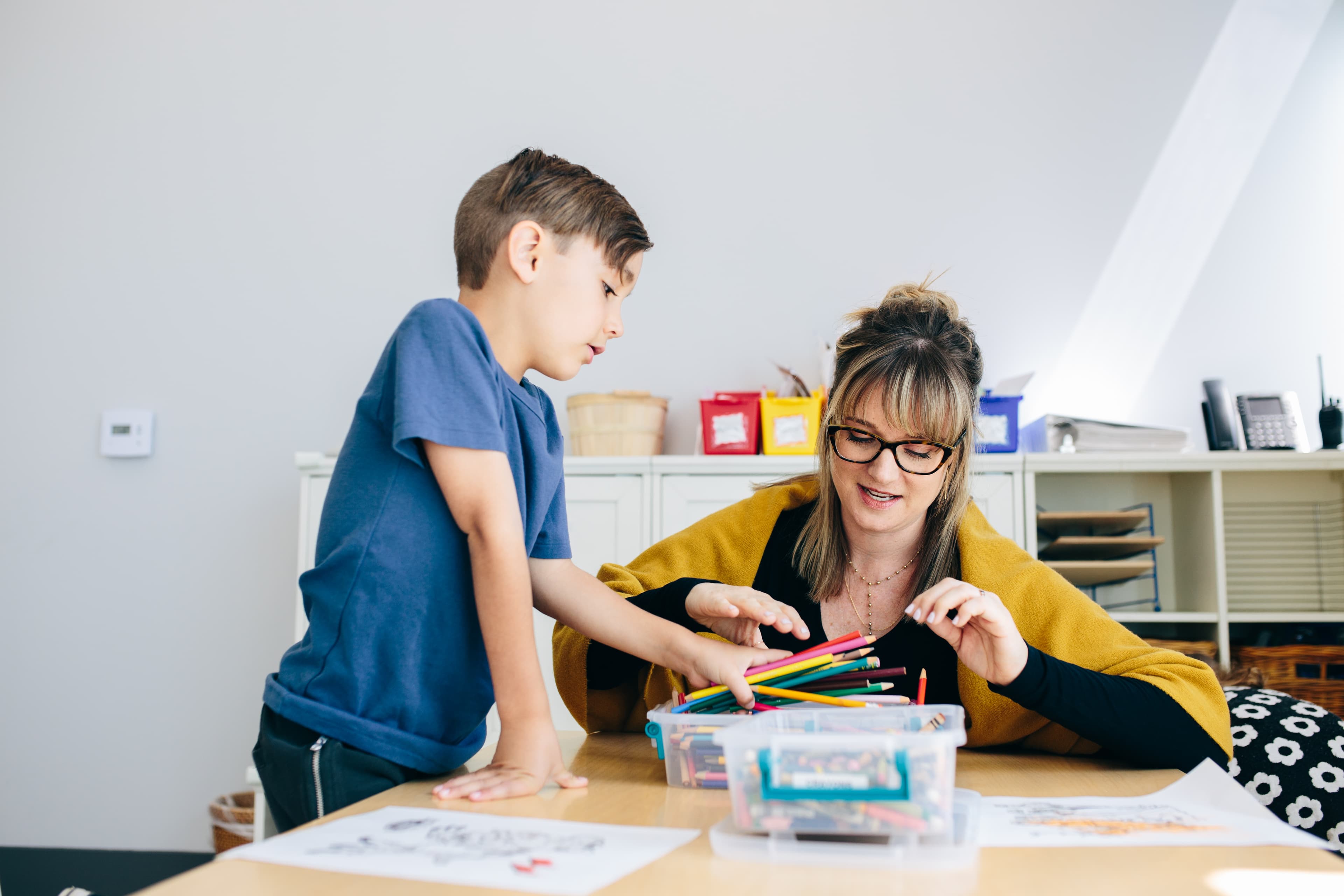 An adult and child playing with colored pencils at a table