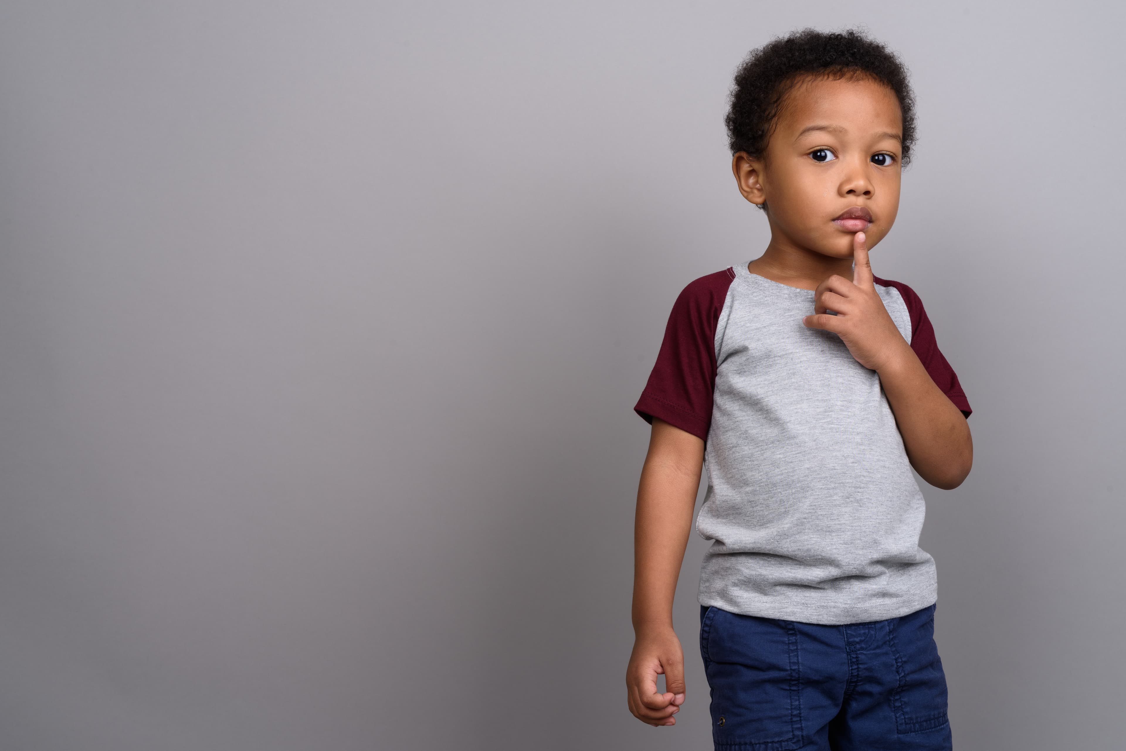 Child holding their finger up to their chin against a gray background