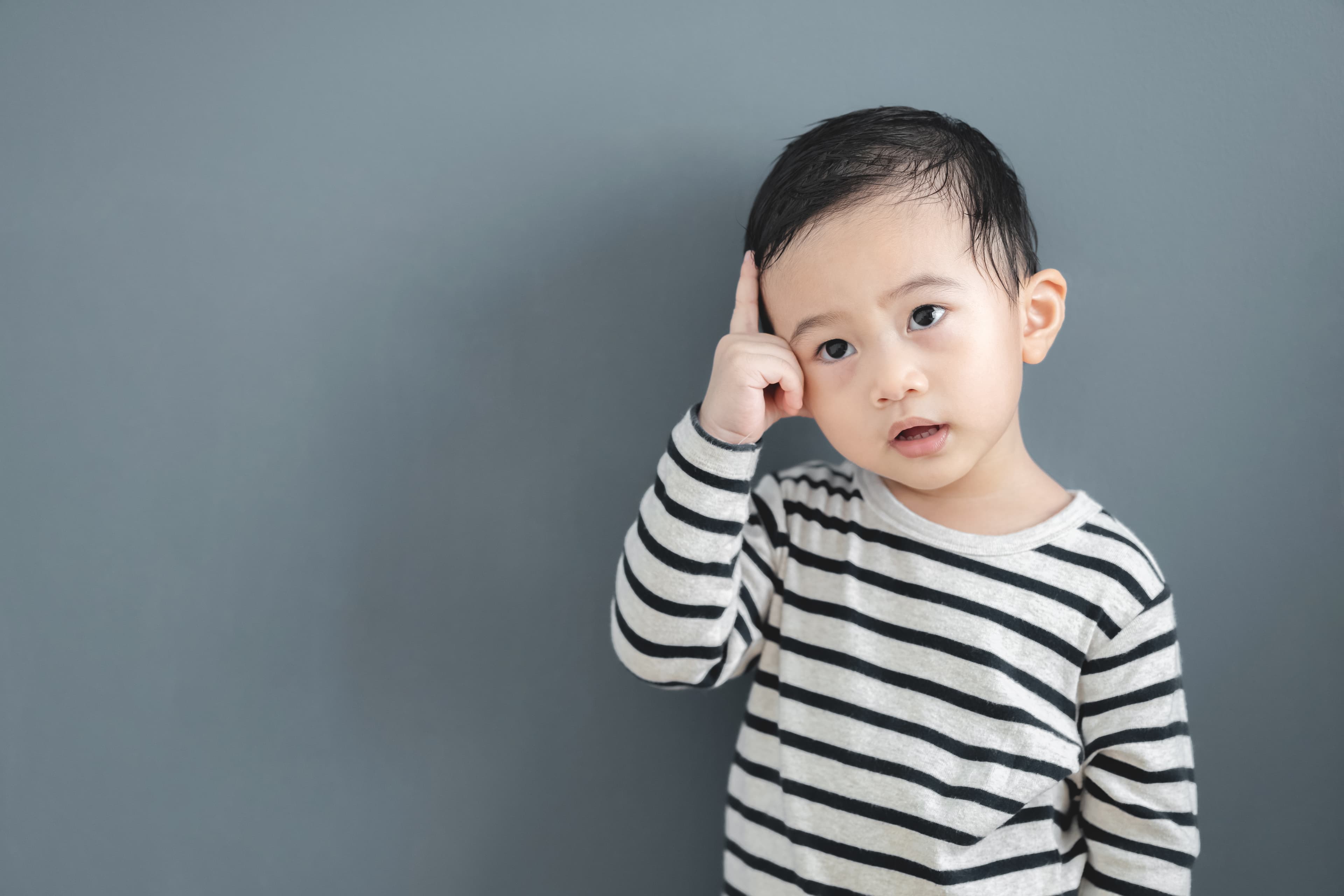 A child holding their hand to the side of their head against a gray background