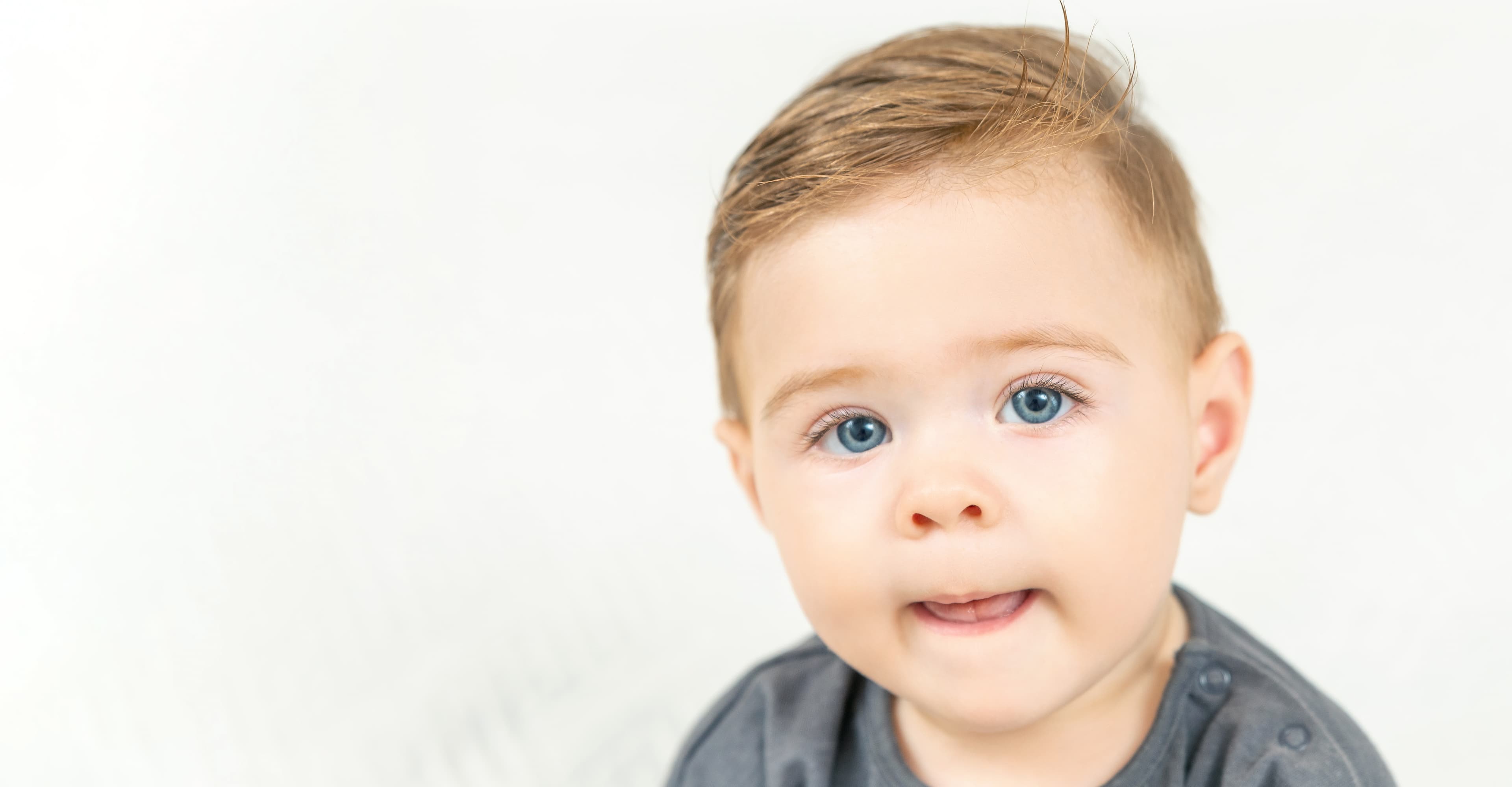 A toddler with blue eyes against a light gray background