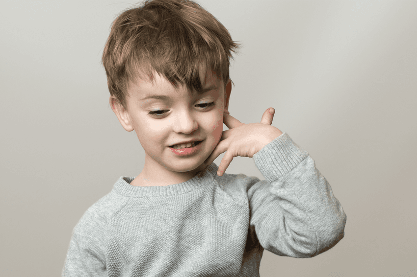 A child holding their hand to their head and looking down with a slight smile
