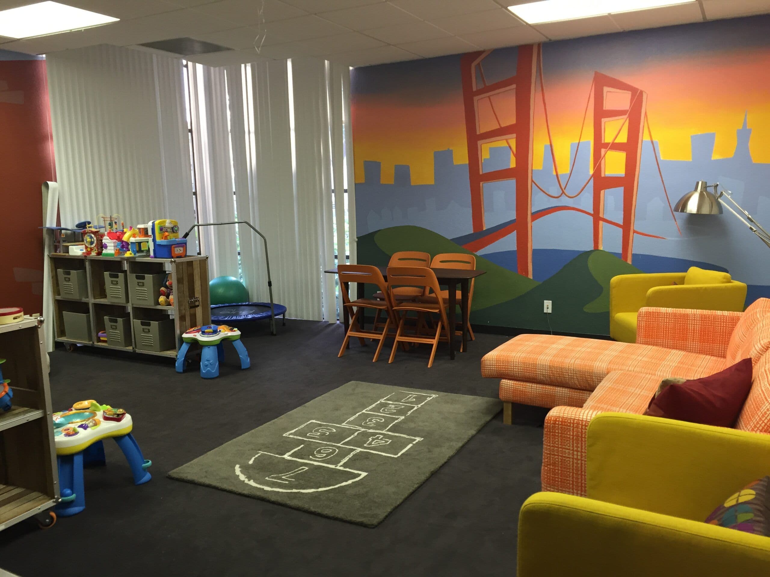 A photo of a kids play area furnished with neatly organized bins of toys. The wallpaper on the far wall depicts the Golden Gate bridge