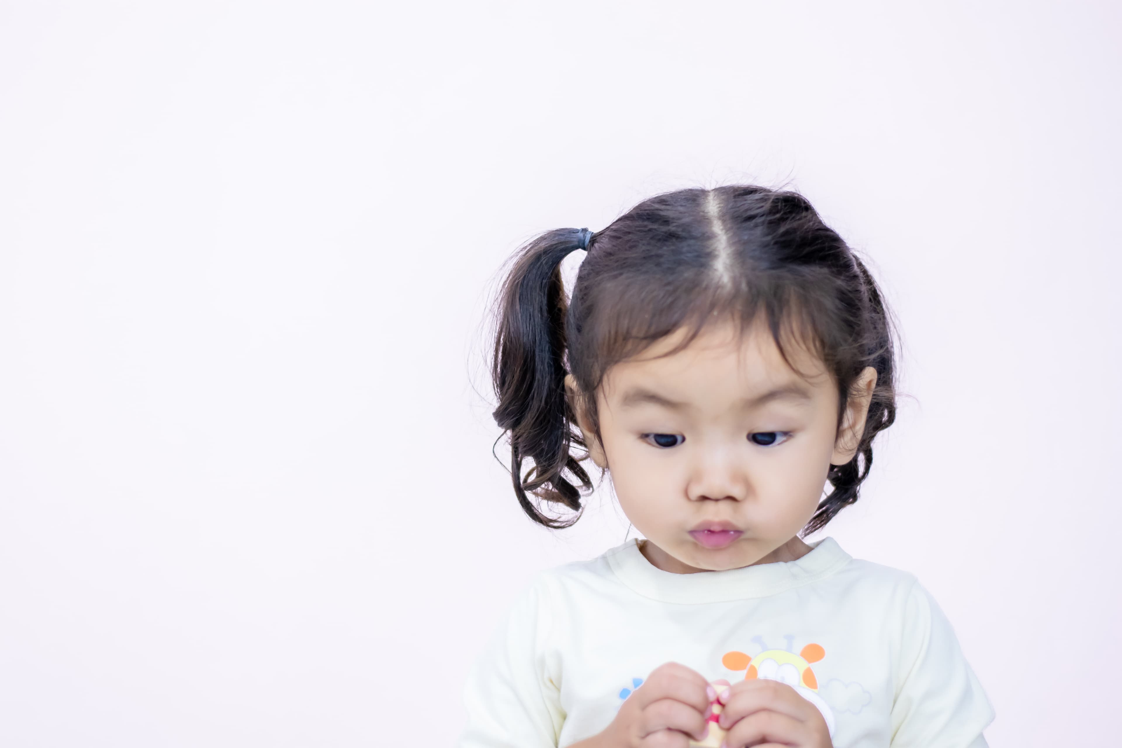 A girl with pursed lips holding her hands together and looking slightly down